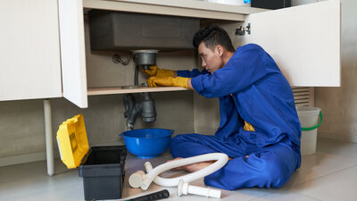 Professional plumber using drain snake to clear clogged drain - Warren Brothers Plumbing serves Bastrop, Austin, and Elgin TX